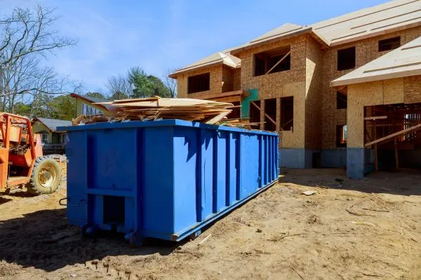 blue dumpster next to an orange tractor in front of a house under construction